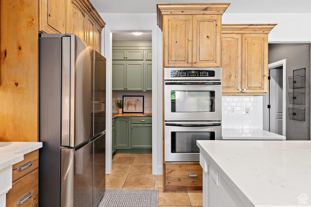 Kitchen featuring stainless steel appliances, backsplash, light tile patterned floors, and green cabinets