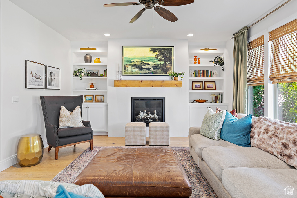 Living room with a ceiling fan, light wood-style floors, a glass covered fireplace, built in shelves, and recessed lighting