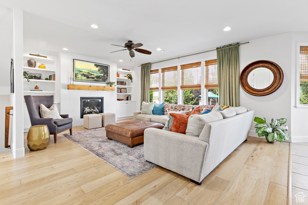 Living area featuring light wood-type flooring, a ceiling fan, built in shelves, recessed lighting, and a glass covered fireplace