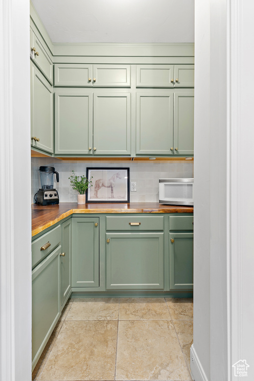 Kitchen with green cabinets, butcher block countertops, white microwave, and tasteful backsplash