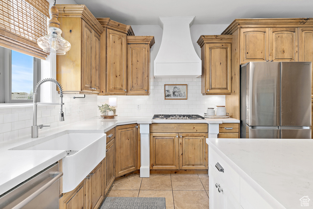 Kitchen with appliances with stainless steel finishes, wall chimney exhaust hood, light countertops, and decorative backsplash