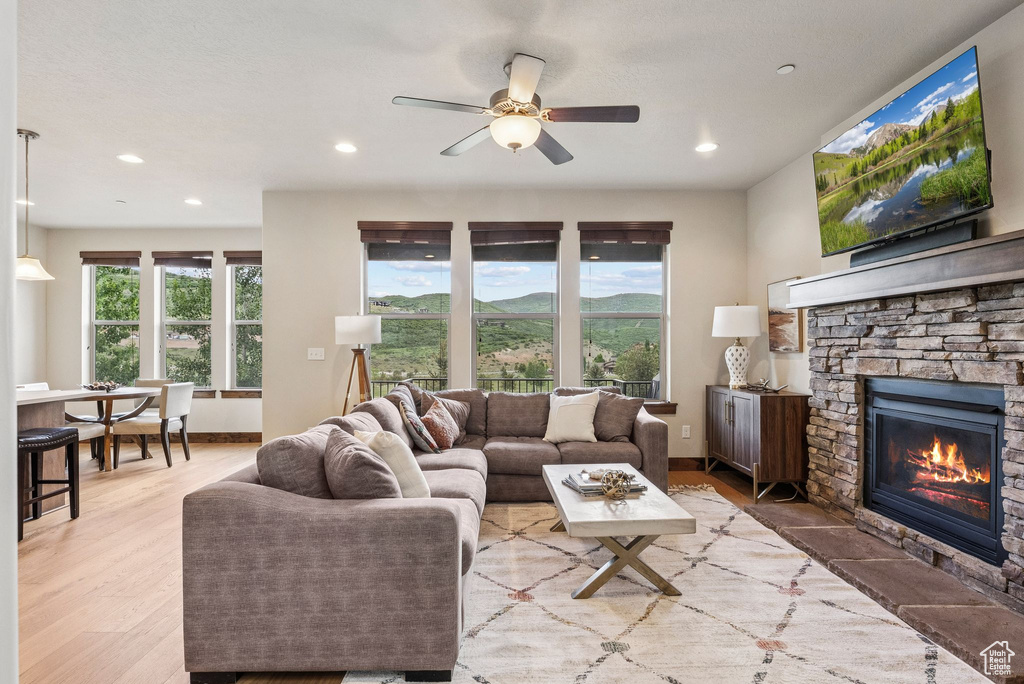 Living room with a stone fireplace, recessed lighting, ceiling fan, and light wood-type flooring