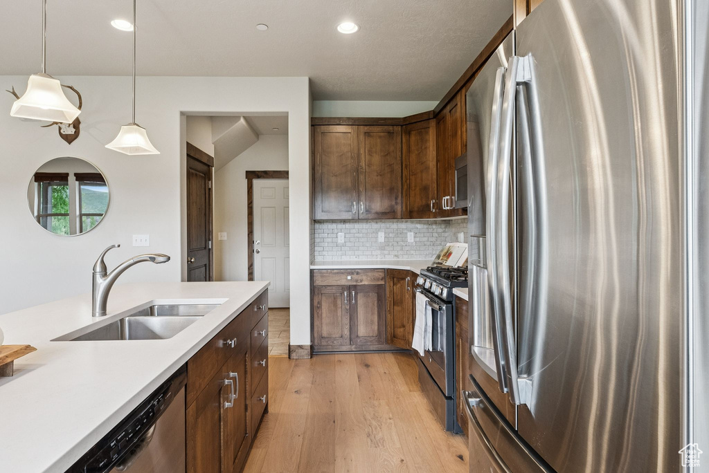 Kitchen featuring appliances with stainless steel finishes, light wood finished floors, light countertops, decorative backsplash, and decorative light fixtures