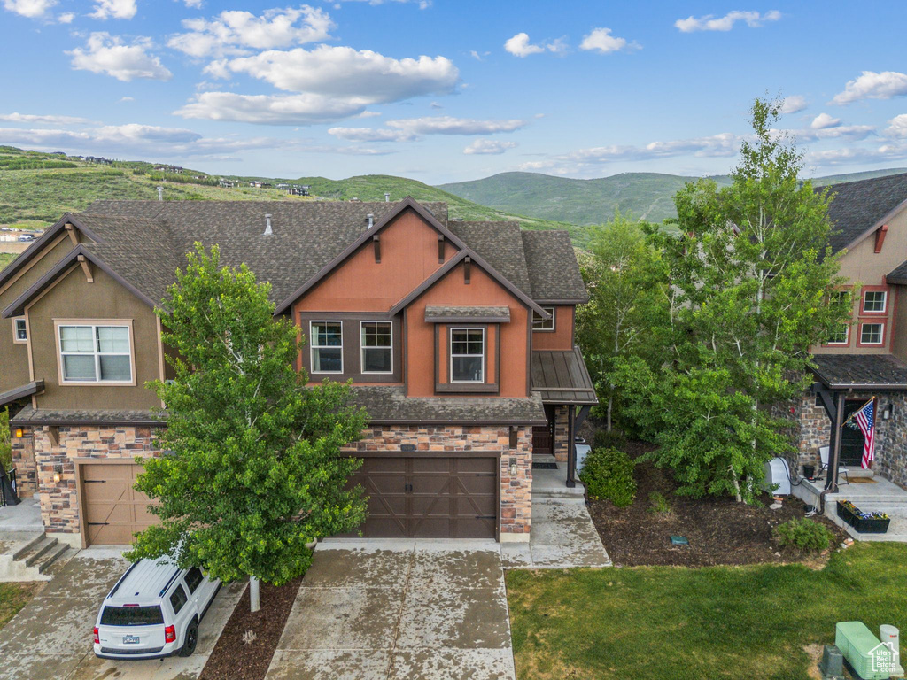 View of front of home featuring stone siding, an attached garage, a mountain view, concrete driveway, and roof with shingles