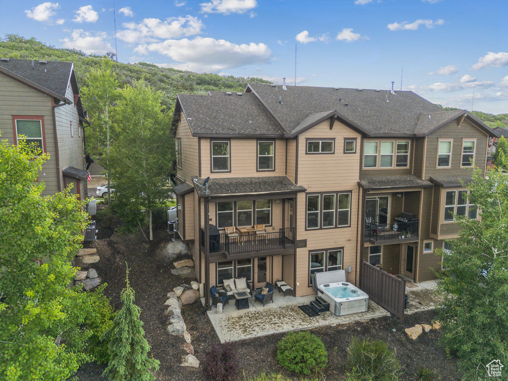 Back of house featuring a patio area, a hot tub, an outdoor living space, and a shingled roof