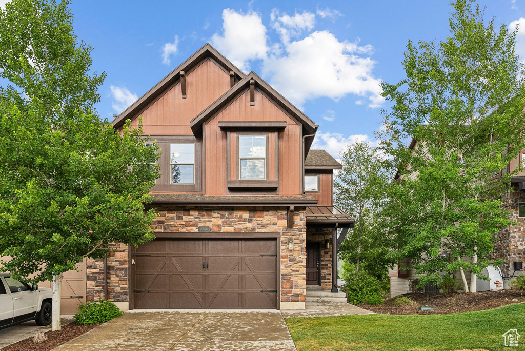 Craftsman-style house featuring stone siding, a garage, concrete driveway, a front yard, and a standing seam roof