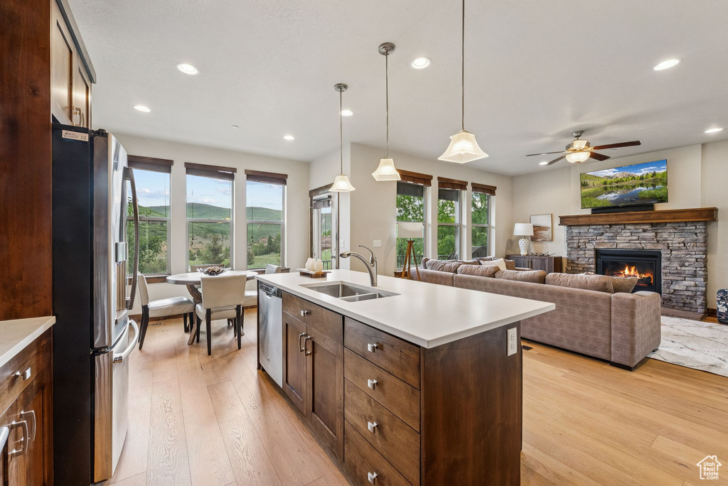 Kitchen with stainless steel appliances, light wood-style floors, light countertops, a stone fireplace, and a ceiling fan