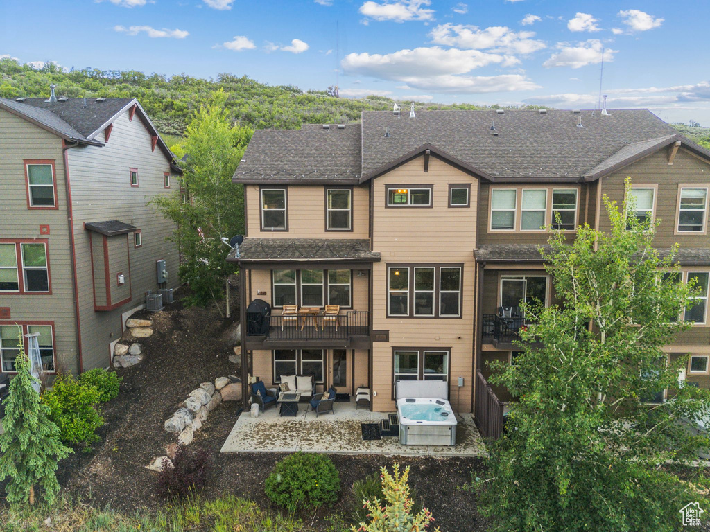 Back of property featuring outdoor lounge area, a patio area, a shingled roof, and a hot tub