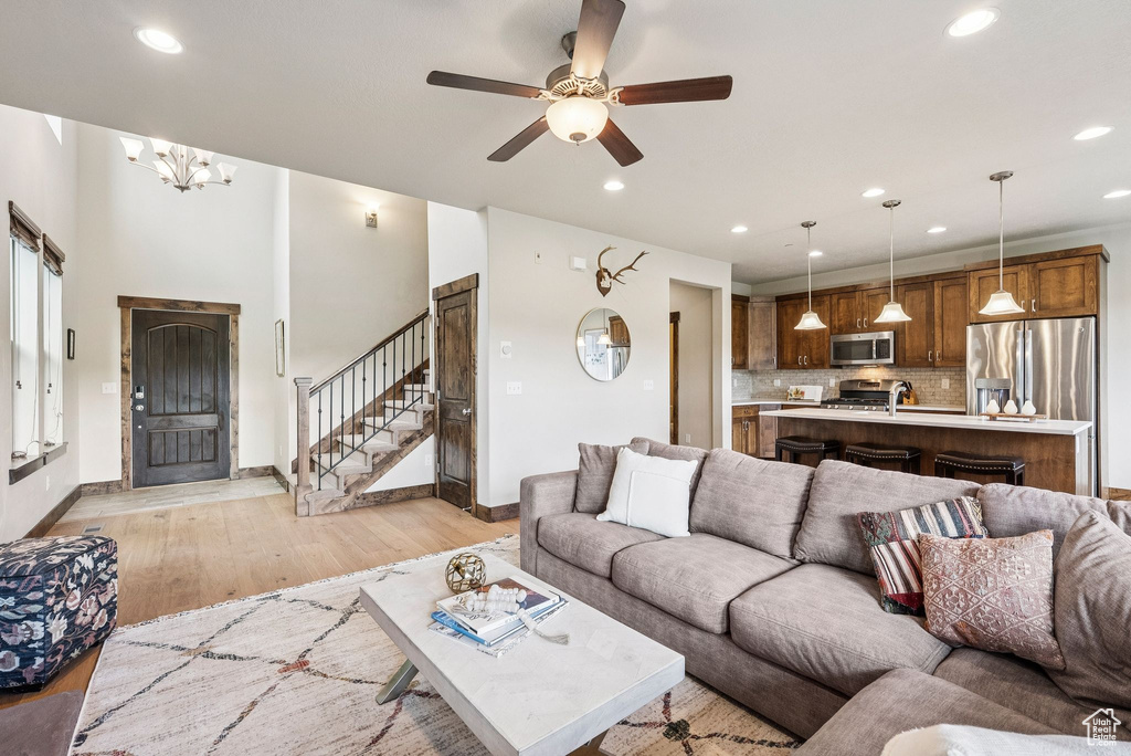 Living room featuring light wood-type flooring, recessed lighting, stairs, a ceiling fan, and a chandelier