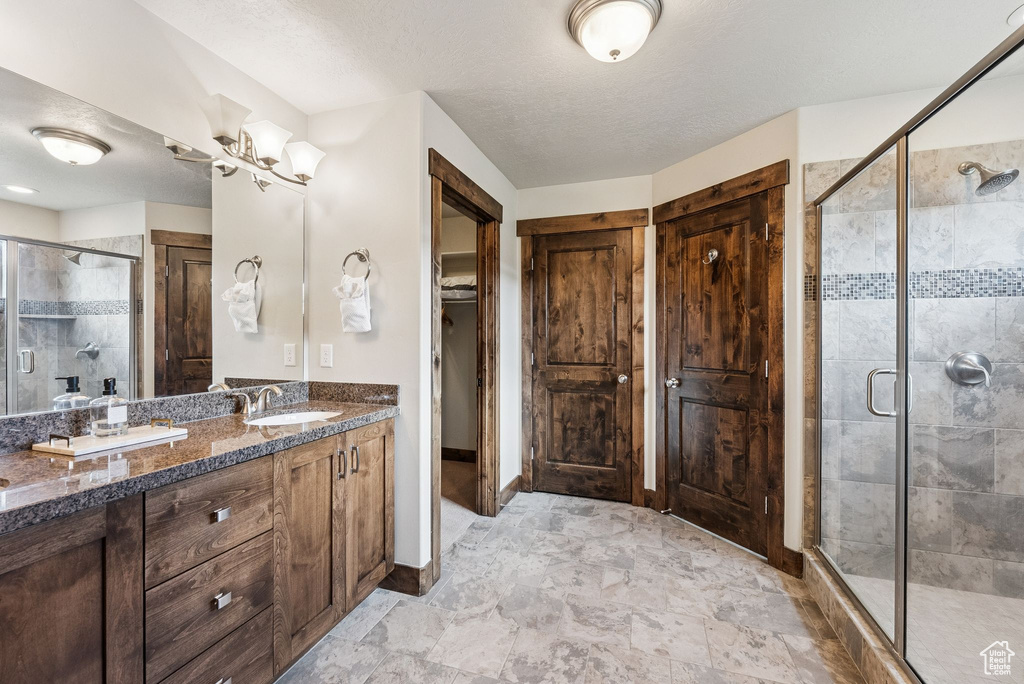 Full bath with a stall shower, double vanity, a chandelier, and a textured ceiling