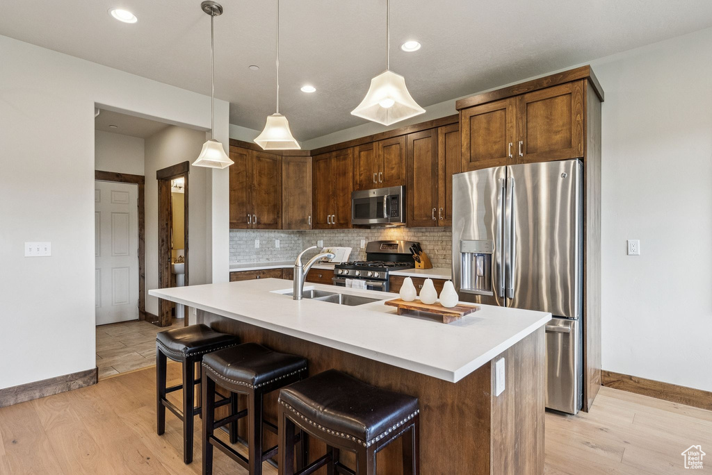 Kitchen featuring stainless steel appliances, tasteful backsplash, light countertops, light wood-type flooring, and recessed lighting