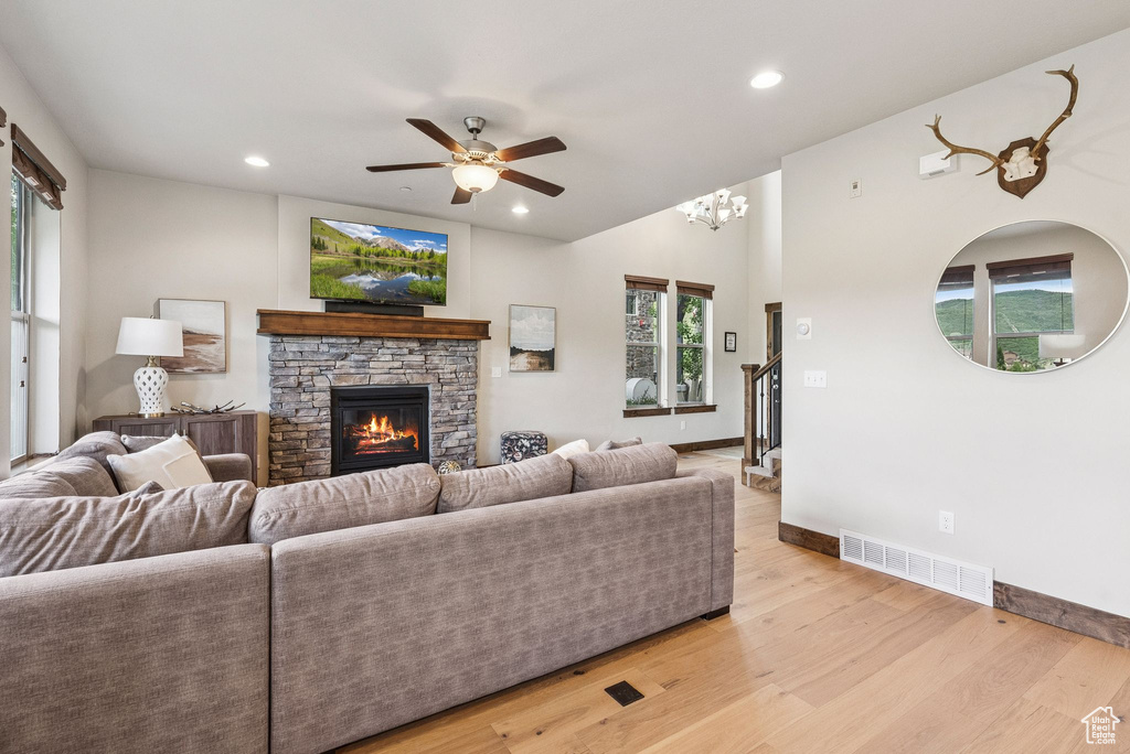 Living room with a ceiling fan, recessed lighting, a stone fireplace, light wood-type flooring, and healthy amount of natural light