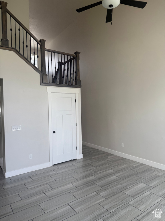 Unfurnished living room featuring ceiling fan, wood tiled floors, a high ceiling, and stairs
