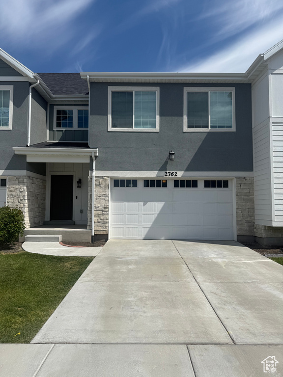 Multi unit property featuring stone siding, an attached garage, concrete driveway, and stucco siding