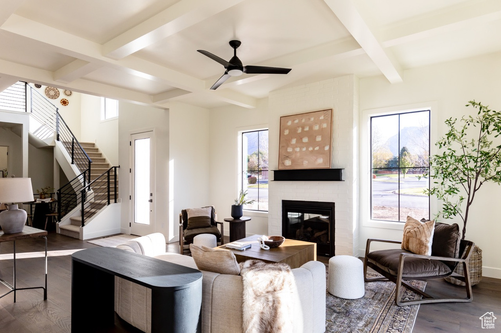 Living room with coffered ceiling, healthy amount of natural light, wood finished floors, a brick fireplace, and beamed ceiling