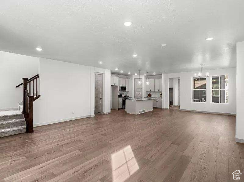 Unfurnished living room featuring wood finished floors, a chandelier, stairway, and recessed lighting