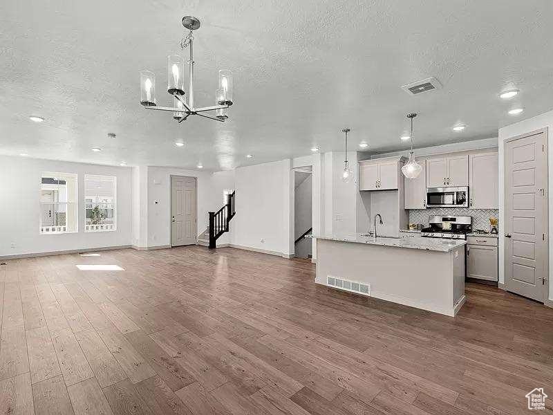 Kitchen with stainless steel appliances, open floor plan, a textured ceiling, a chandelier, and wood finished floors