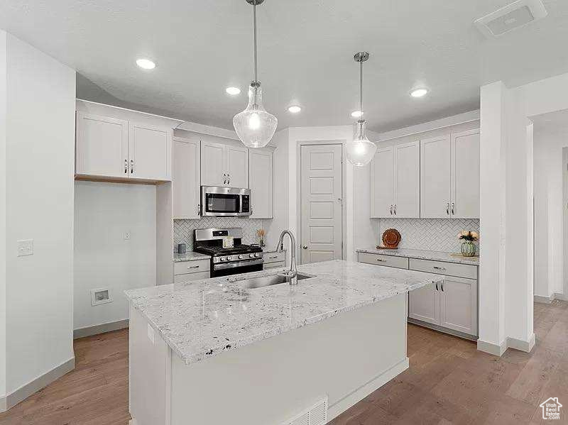 Kitchen with stainless steel appliances, light wood-style flooring, recessed lighting, and backsplash