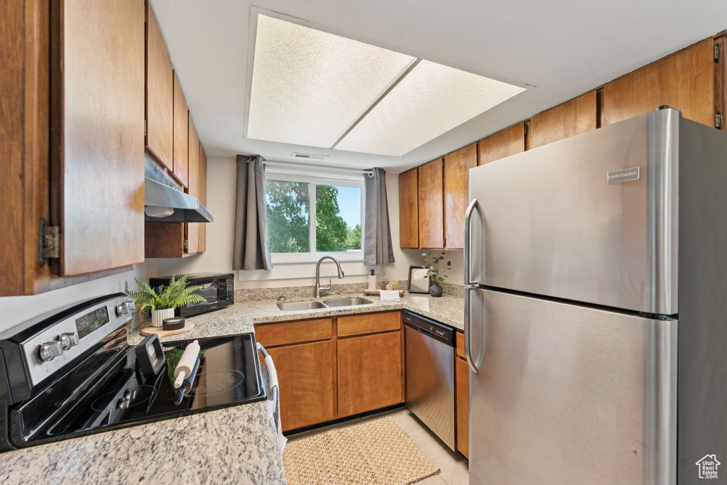 Kitchen with appliances with stainless steel finishes, under cabinet range hood, and brown cabinetry