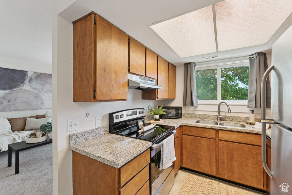 Kitchen with appliances with stainless steel finishes, under cabinet range hood, brown cabinetry, and light stone countertops