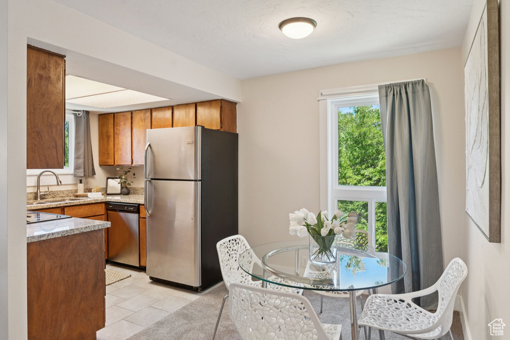 Kitchen with stainless steel appliances, brown cabinets, light tile patterned floors, and light stone countertops
