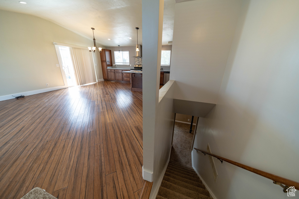 Unfurnished living room with dark wood finished floors, vaulted ceiling, and a chandelier