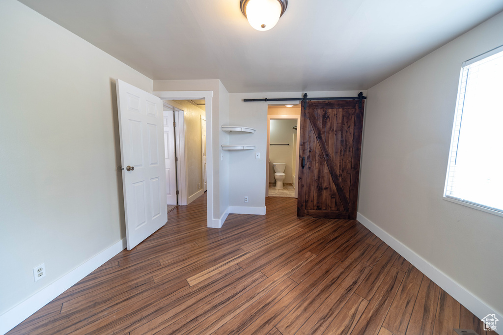 Unfurnished bedroom featuring dark wood-style flooring, a barn door, and multiple windows