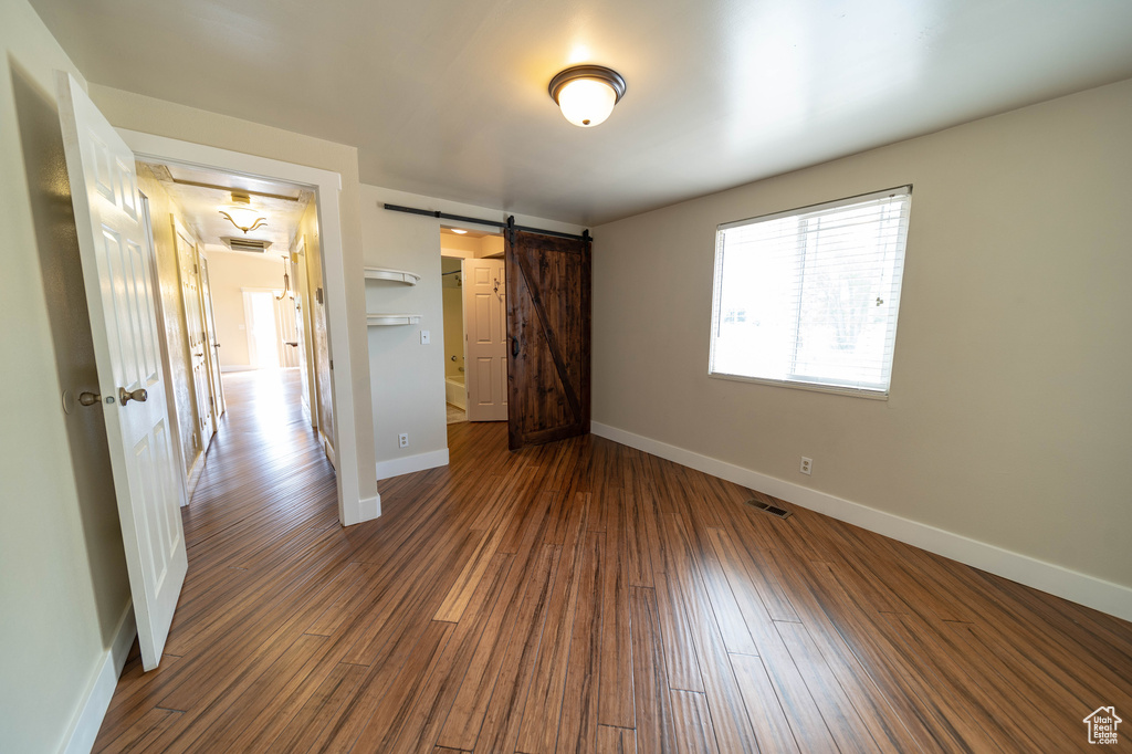 Unfurnished bedroom featuring dark wood-style flooring and a barn door