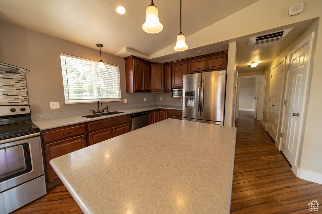Kitchen featuring stainless steel appliances, dark wood finished floors, light countertops, a kitchen island, and hanging light fixtures