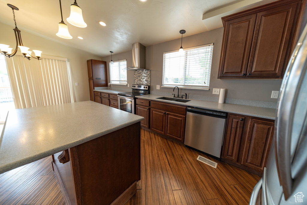 Kitchen featuring appliances with stainless steel finishes, wall chimney range hood, dark wood-style floors, recessed lighting, and pendant lighting