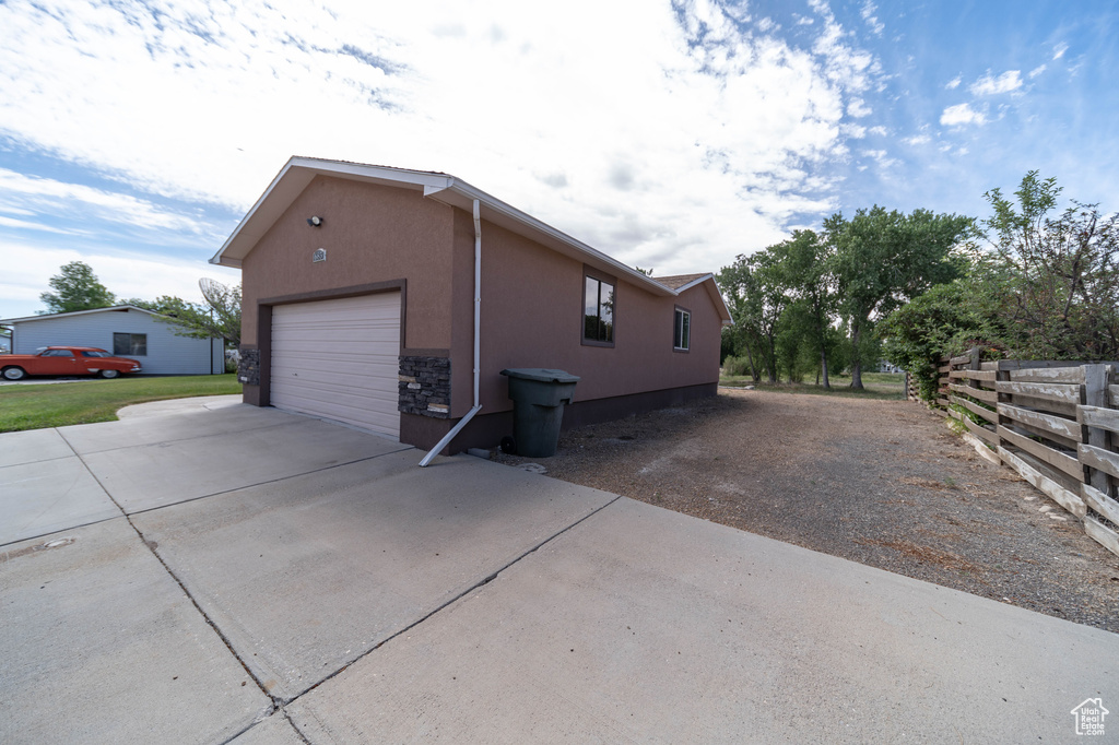 View of side of home featuring concrete driveway, stucco siding, and stone siding
