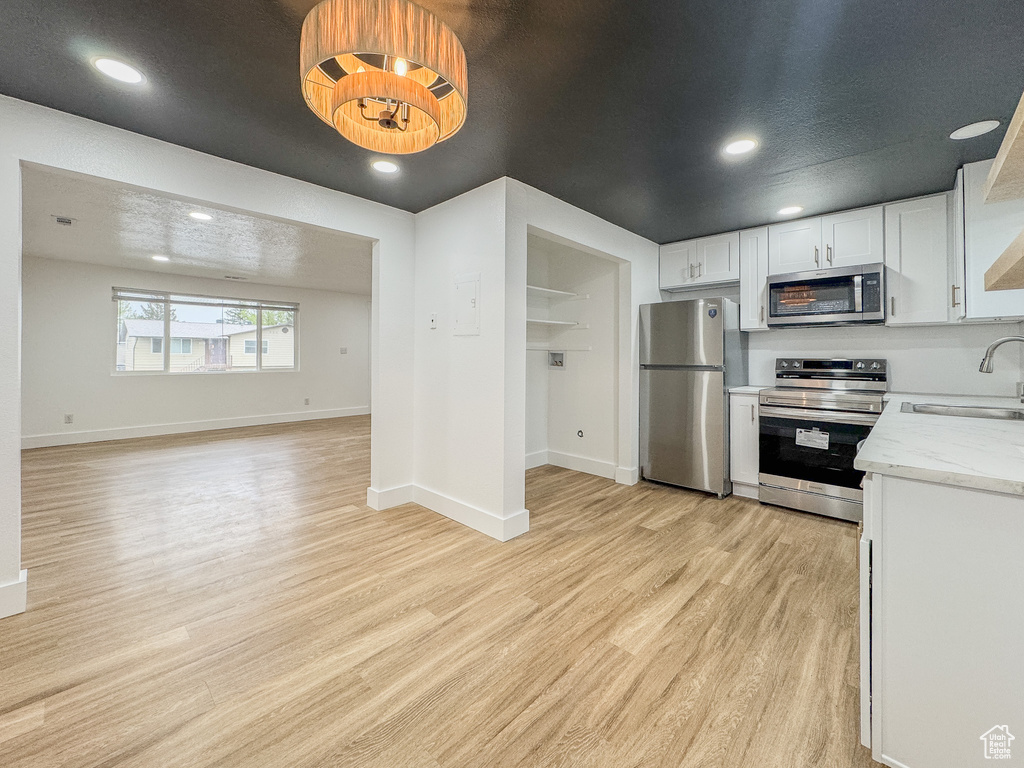 Kitchen featuring stainless steel appliances, light wood-style floors, white cabinets, recessed lighting, and open floor plan