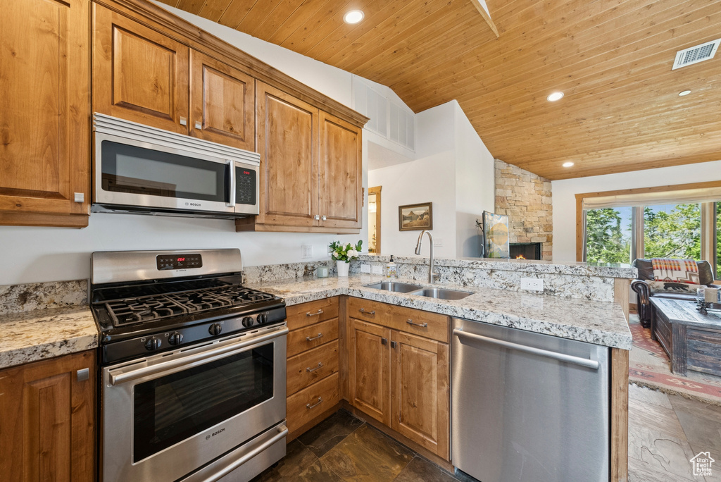 Kitchen with appliances with stainless steel finishes, wood ceiling, a peninsula, brown cabinetry, and vaulted ceiling