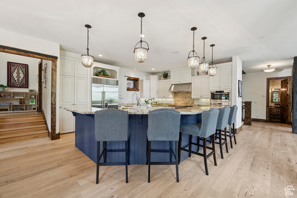 Kitchen with stainless steel built in fridge, white cabinetry, tasteful backsplash, light wood-type flooring, and recessed lighting