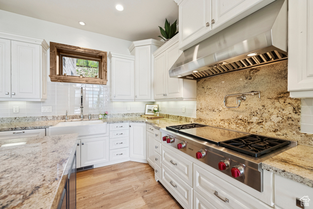 Kitchen with under cabinet range hood, stainless steel gas cooktop, tasteful backsplash, white cabinetry, and recessed lighting
