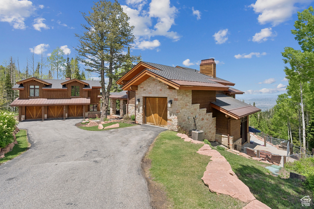 View of front of property featuring stone siding, a chimney, asphalt driveway, and a garage