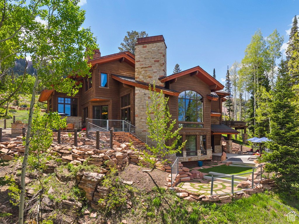 Rear view of house with a patio area, a chimney, stone siding, and a metal roof