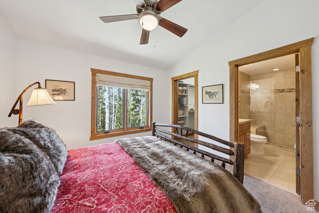 Carpeted bedroom featuring lofted ceiling, connected bathroom, tile patterned flooring, and a ceiling fan
