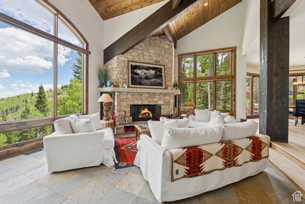 Living area with a wooden ceiling with exposed beams, high vaulted ceiling, healthy amount of natural light, and a stone fireplace
