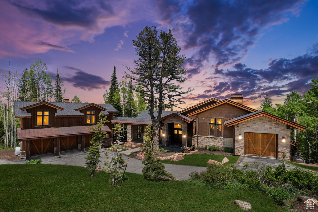 Contemporary home with a chimney, driveway, stone siding, an attached garage, and a lawn