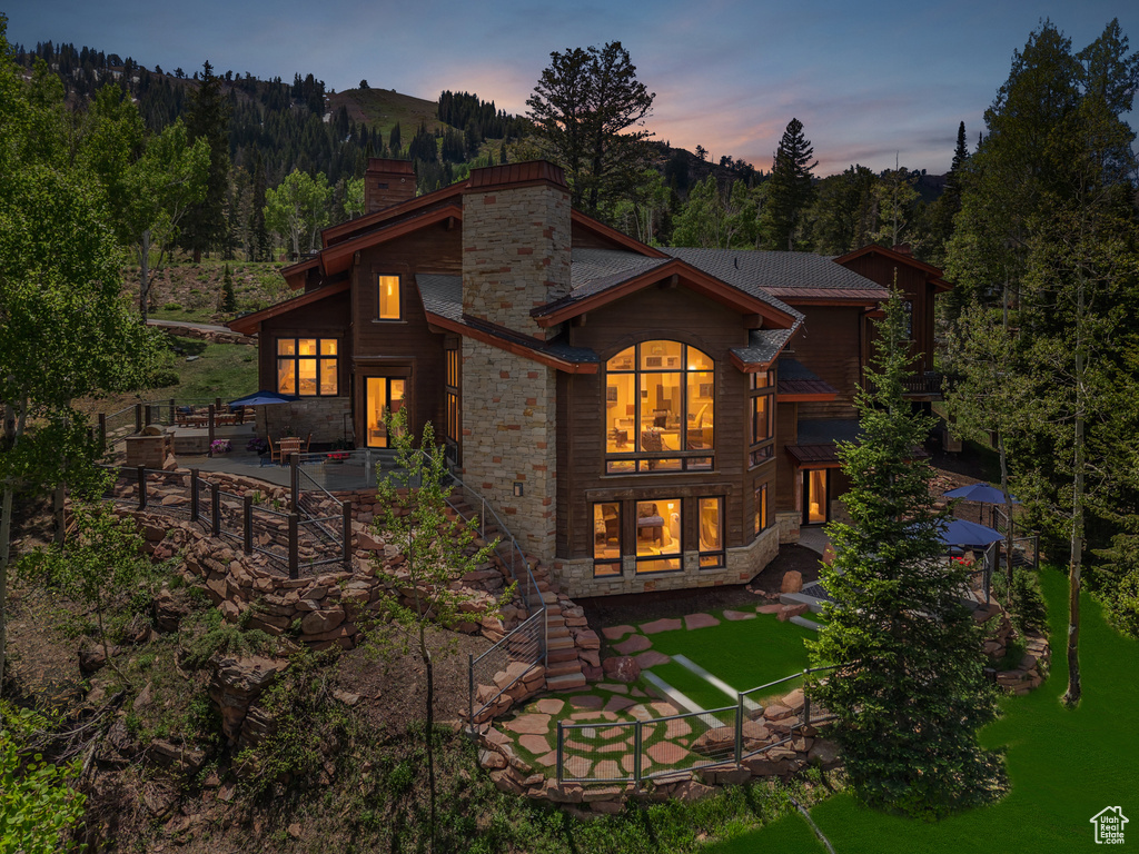 Back of property at dusk featuring a chimney, a patio area, and stone siding