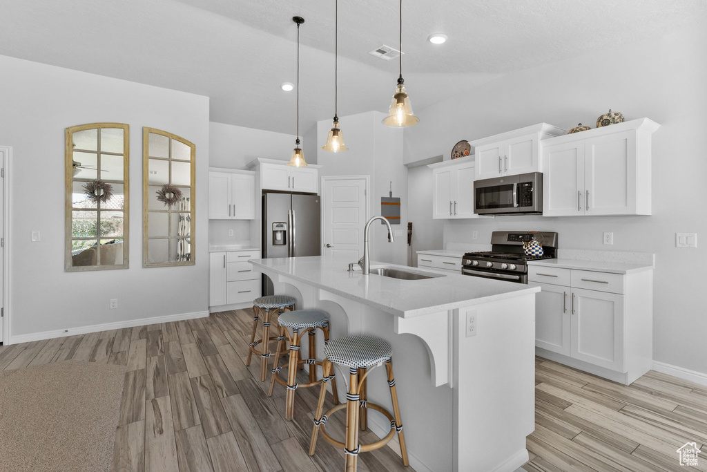 Kitchen with stainless steel appliances, light wood-style flooring, light countertops, a breakfast bar, and a center island with sink
