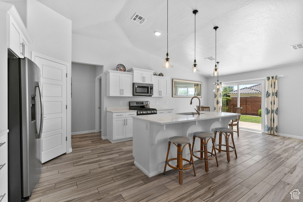 Kitchen featuring stainless steel appliances, light wood-style floors, light countertops, white cabinets, and vaulted ceiling