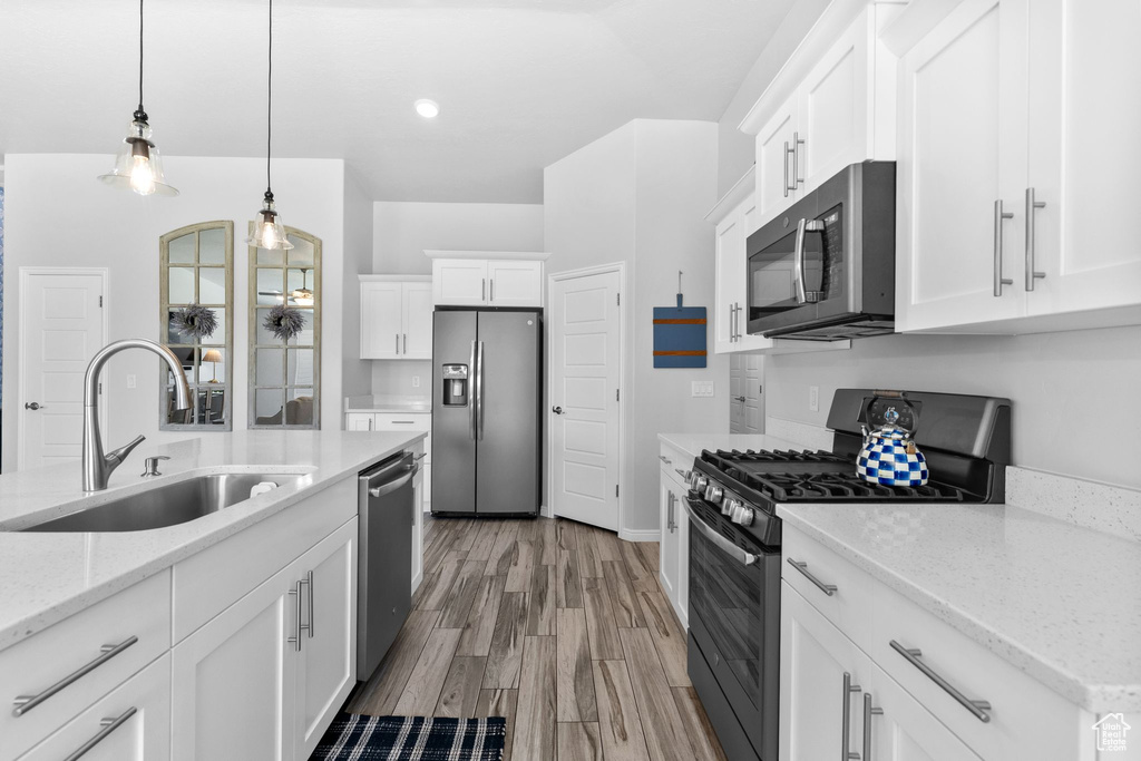 Kitchen featuring stainless steel appliances, white cabinets, hanging light fixtures, light wood finished floors, and recessed lighting