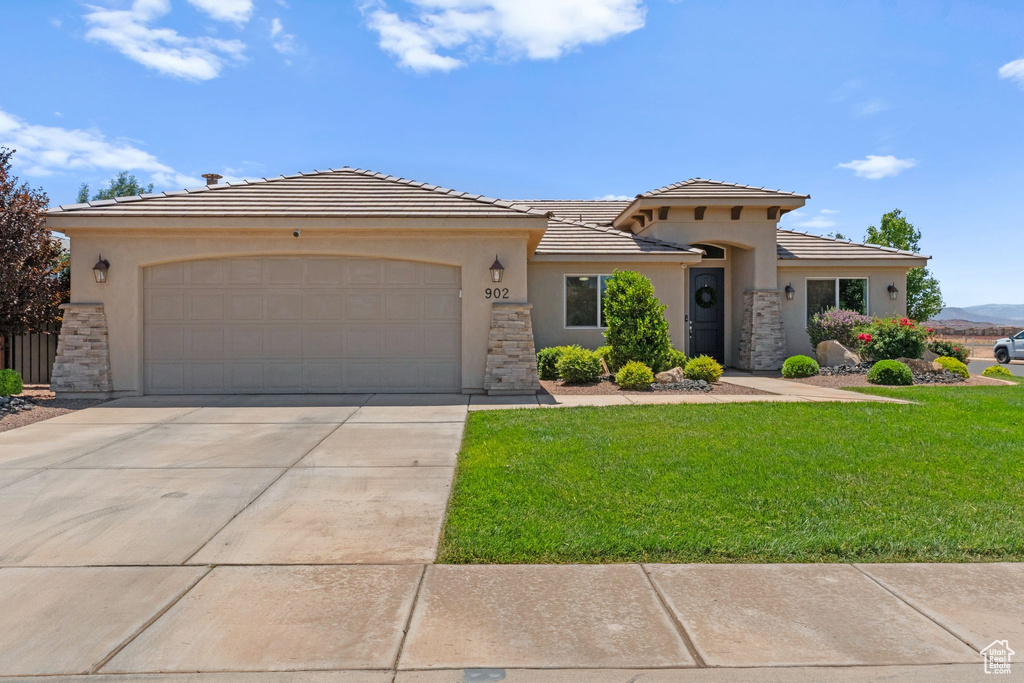 View of front facade with stucco siding, a front yard, an attached garage, and driveway