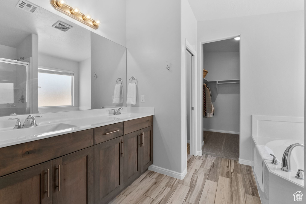 Full bath featuring a shower stall, double vanity, a garden tub, a walk in closet, and wood finished floors
