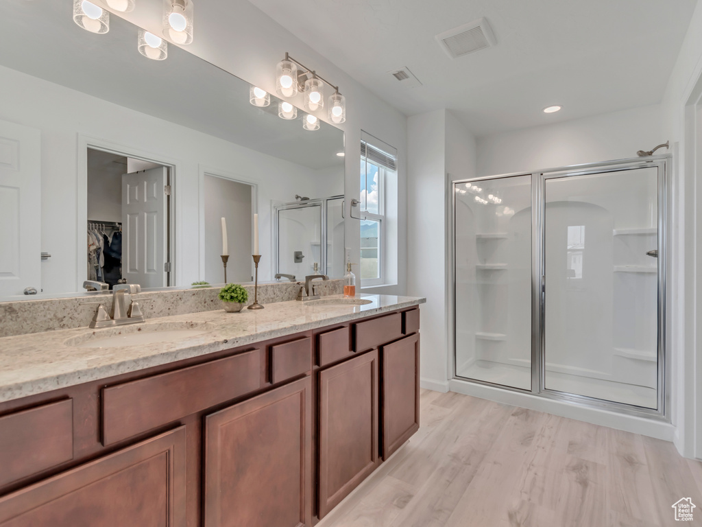 Bathroom with a stall shower, a spacious closet, double vanity, and wood finished floors