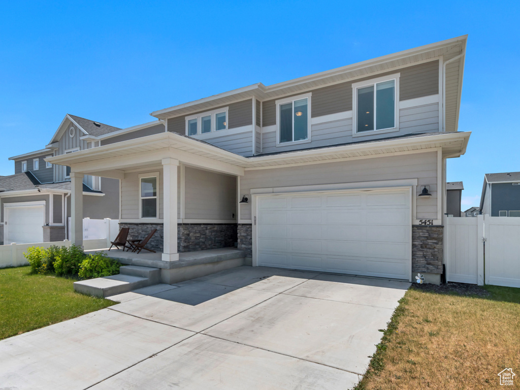 View of front of property featuring a porch, stone siding, an attached garage, and driveway