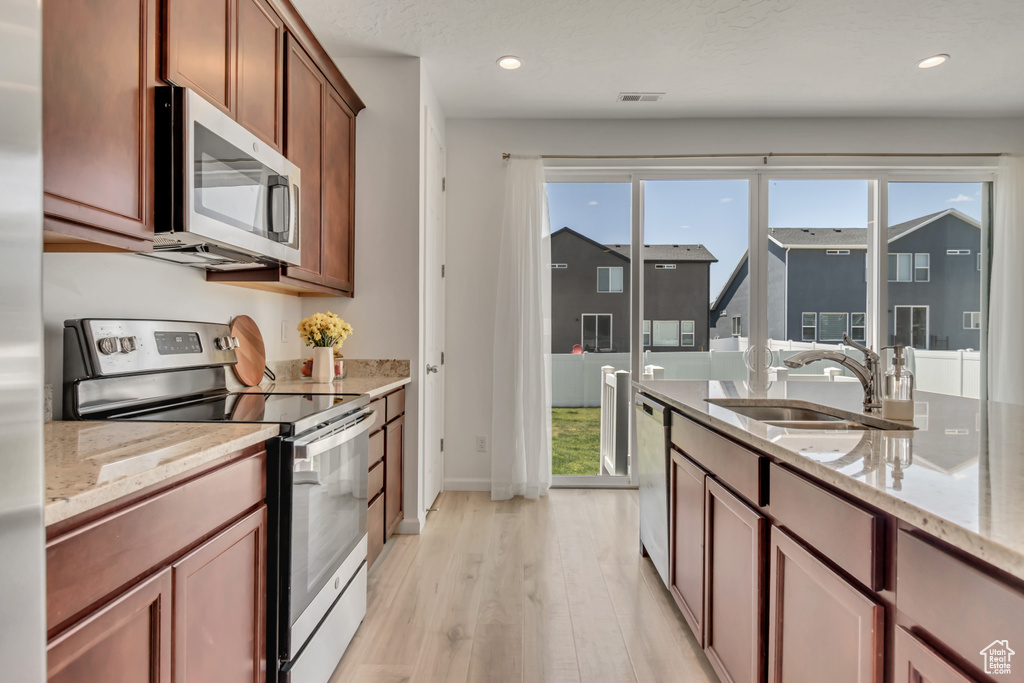 Kitchen featuring appliances with stainless steel finishes, light wood-type flooring, recessed lighting, light stone countertops, and brown cabinets