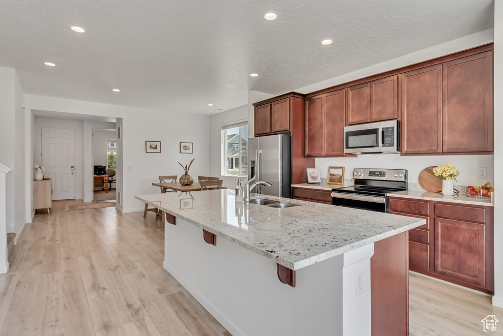 Kitchen featuring appliances with stainless steel finishes, a kitchen breakfast bar, light wood finished floors, an island with sink, and recessed lighting